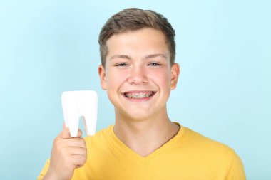 Diş teli takan genç bir adam mavi sırtında diş modelini tutuyor.