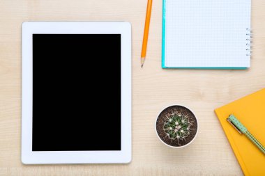 Kahverengi ahşap masa üzerinde not defterleri ve kaktüsü olan tablet bilgisayar.