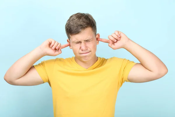 Giovane uomo che chiude le orecchie con le dita su sfondo blu — Foto Stock