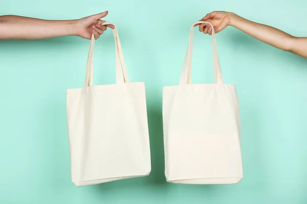 Mains féminines tenant des sacs éco en coton blanc sur fond menthe — Photo