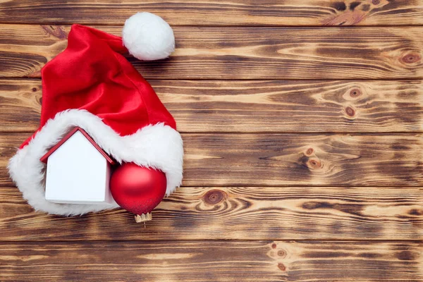 Rode kerstmuts met huismodel en kerstbal op bruin houten b — Stockfoto