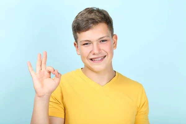 Junger Mann mit Zahnspange zeigt Okay-Geste auf blauem Rücken — Stockfoto