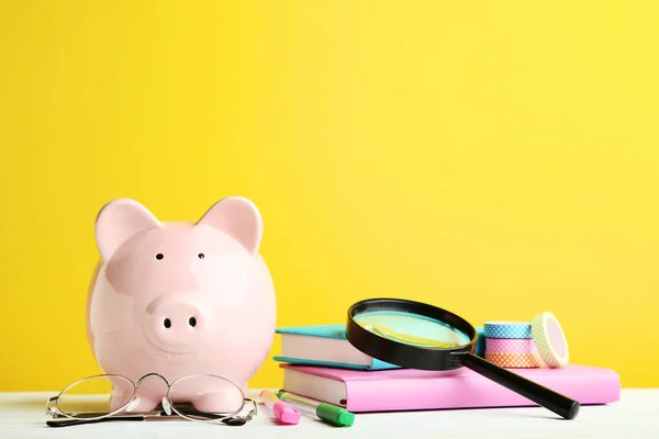 Piggy bank rosa com livros e lupa no backgr amarelo — Fotografia de Stock