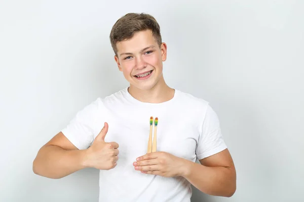 Młody człowiek trzyma szczoteczki do zębów i pokazuje kciuk na szarym grzbiecie — Zdjęcie stockowe