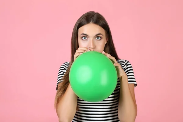 Young woman blowing green balloon on pink background