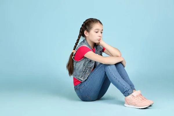 Ledsen ung flicka sitter på blå bakgrund — Stockfoto