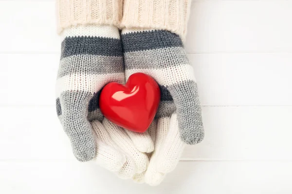 Hände in Strickhandschuhen mit Herz auf weißem Holztisch — Stockfoto