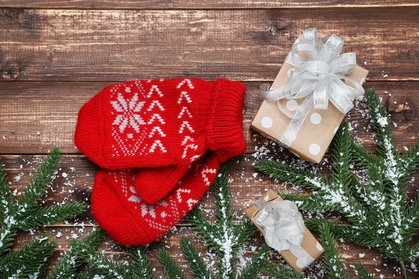 Knitted mittens with fir tree branches and gift box on wooden ta