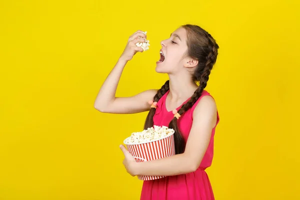 Hermosa joven comiendo palomitas de maíz sobre fondo amarillo —  Fotos de Stock