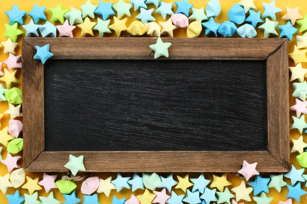 Barevné papírové hvězdy s dřevěným rámem na žlutém pozadí — Stock fotografie