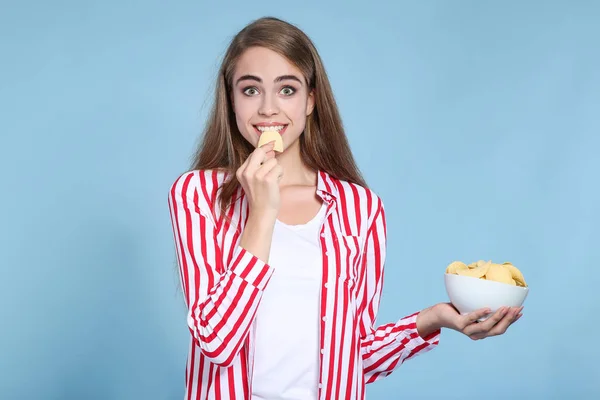 Młoda piękna dziewczyna je chipsy ziemniaczane na niebieskim tle — Zdjęcie stockowe