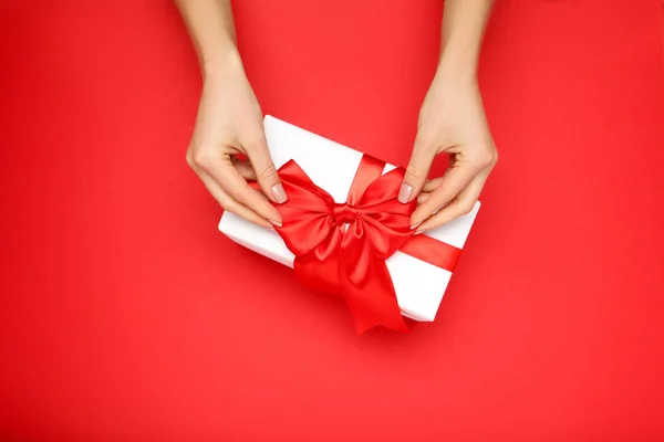 Gift box with ribbon and female hands on red background — Stock Photo, Image