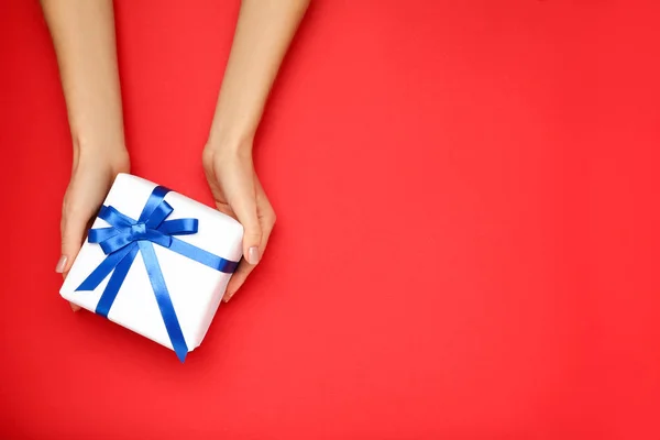 Gift box with ribbon in female hands on red background — Stock Photo, Image