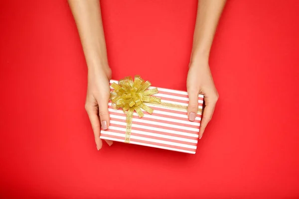 Caixa de presente com fita em mãos femininas sobre fundo vermelho — Fotografia de Stock