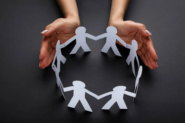 Female hands protecting paper chain people on black background — Stock Photo, Image