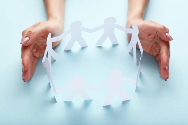 Female hands protecting paper chain people on blue background — Stock Photo, Image