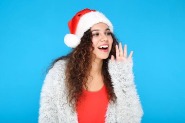 Güzel Amerikalı kadın Noel Baba şapkası takıyor ve mavi arka planda çığlık atıyor.