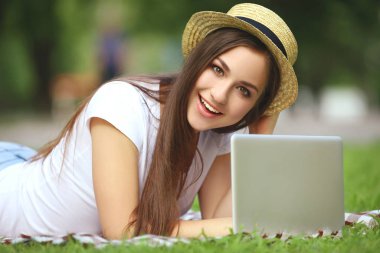 Dizüstü bilgisayarı olan şapkalı genç kız çimlerin üzerinde yatıyordu.