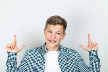 Diş teli takan genç adam gri arka planda parmaklarını gösteriyor.