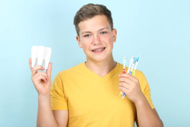 Mavi arka planda diş fırçası ve diş modeli olan genç bir adam.