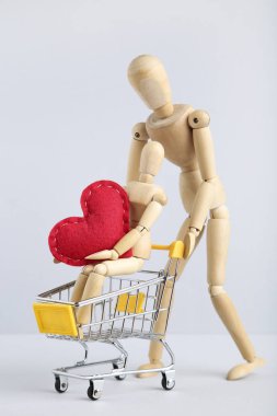 Kırmızılı ahşap aile figürleri ve gri arka planda alışveriş arabası.