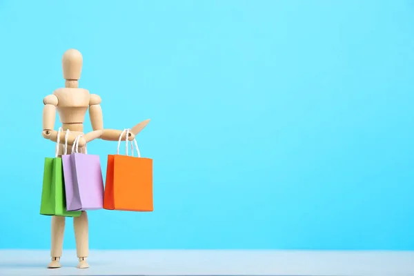 Деревянная фигура с бумажными пакетами покупок на синем фоне — стоковое фото