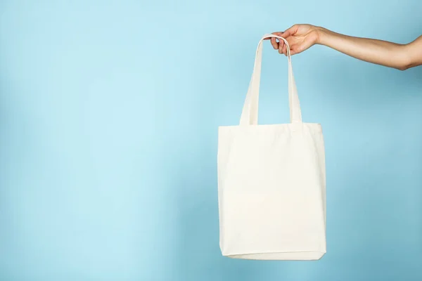 Γυναικείο χέρι κρατώντας λευκό βαμβάκι eco bag σε μπλε φόντο — Φωτογραφία Αρχείου