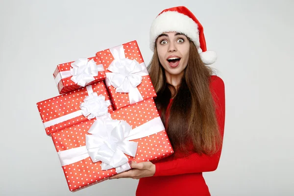 Mulher bonita usando chapéu de Papai Noel e segurando caixas de presente em cinza — Fotografia de Stock