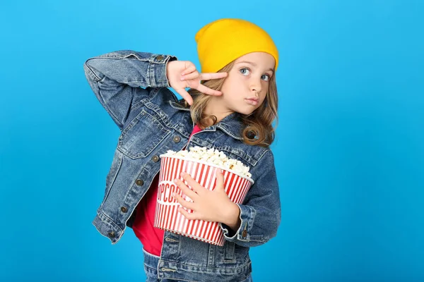 Young girl holding bucket with popcorn on blue background