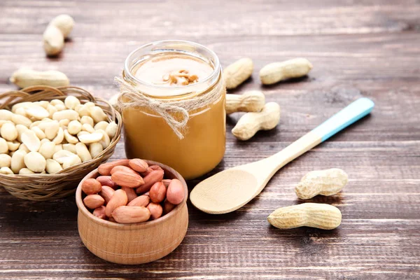 Peanut butter in jar and nuts on brown wooden table