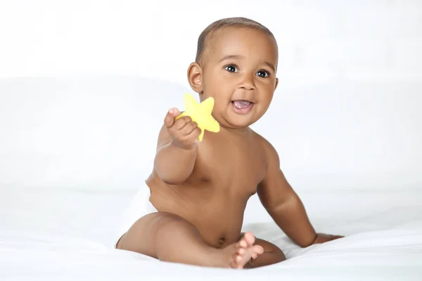 美国女婴坐在白色的床上 手里拿着黄色的玩具 — 图库照片