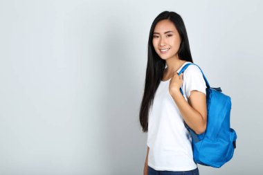 Gri arka planda sırt çantası olan güzel genç bir kadın.