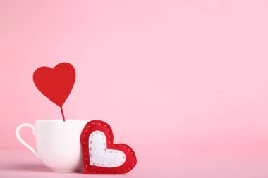 Kumaş ve ahşap kalpler, pembe arka planda beyaz bardak.