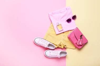 Renkli arka planda aksesuarları ve parfüm şişesi olan moda kadın kıyafetleri.