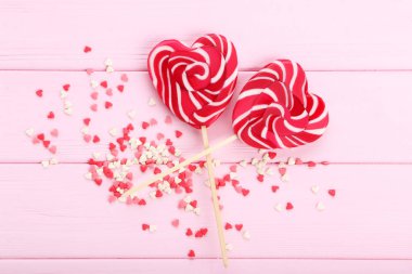 Kalp şeklinde lolipoplar pembe ahşap masaya serpiştirilmiş.