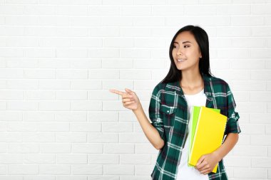 Beyaz tuğla duvar arkasında not defterleri olan genç bir kadın.