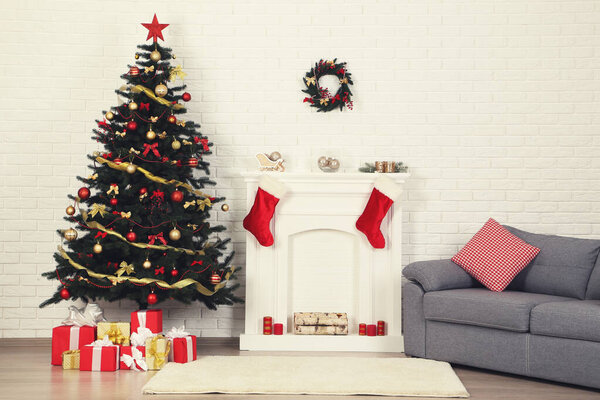 Christmas fir tree with ornaments and gift boxes near decorated fireplace at home
