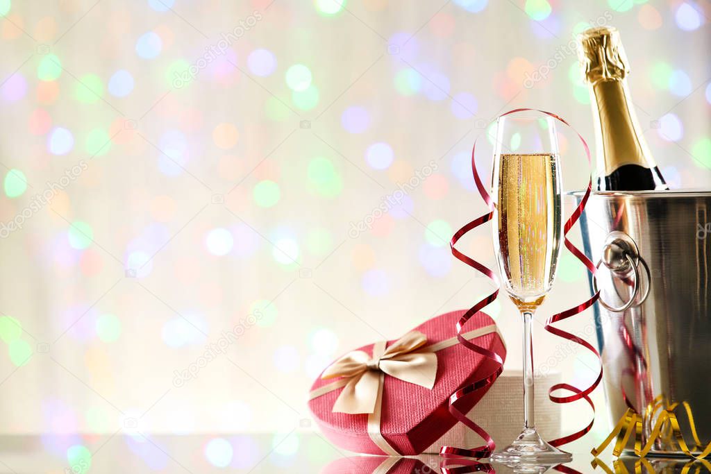 Bottle and glass of champagne with gift box on blurred lights background