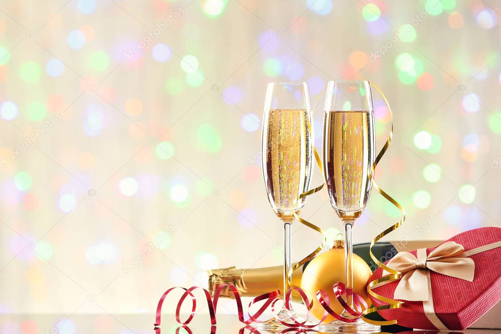 Glasses of champagne with bottle and gift box on blurred lights background