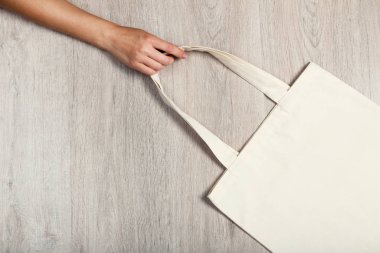 Ahşap arka planda beyaz pamuklu eko çanta tutan bir kadın.