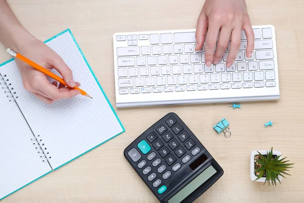 Manos femeninas escribiendo en el teclado de la computadora con bloc de notas y calculo —  Fotos de Stock