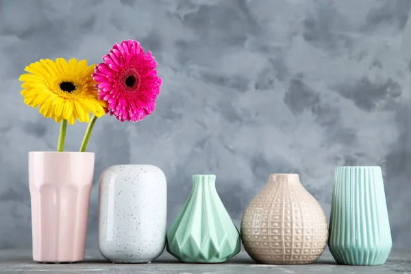 Різні керамічні вази з квітами гербери на сірому фоні — стокове фото