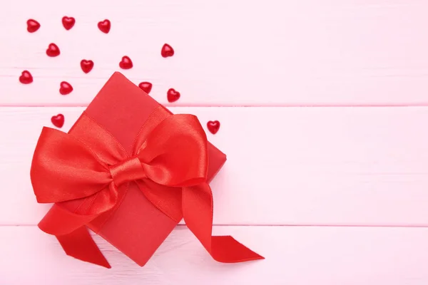 Gift box with ribbon bow and red hearts on pink wooden table — Stock Photo, Image