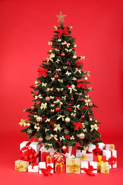 Árbol de abeto de Navidad con adornos y cajas de regalo en el fondo rojo — Foto de Stock