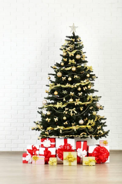 Karácsonyi fenyő díszekkel és ajándékdobozokkal fehér téglán — Stock Fotó