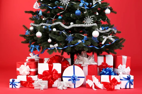 Sapin de Noël avec des ornements et des boîtes-cadeaux sur fond rouge — Photo