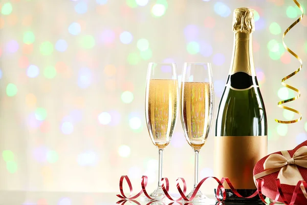 Botella y copas de champán con caja de regalo en luces borrosas —  Fotos de Stock