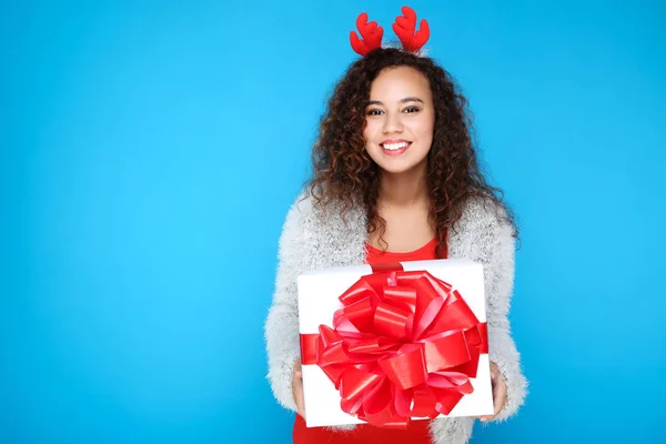 Gyönyörű amerikai nő piros szarvú gazdaság ajándék doboz kék háttér — Stock Fotó