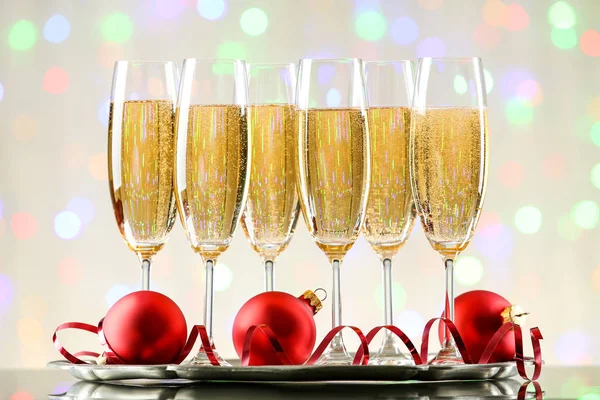 Glasses of champagne with red baubles and ribbon on blurred ligh — Stock Photo, Image
