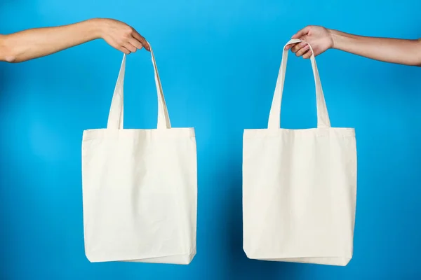 Mains féminines tenant des sacs écologiques en coton blanc sur fond bleu — Photo